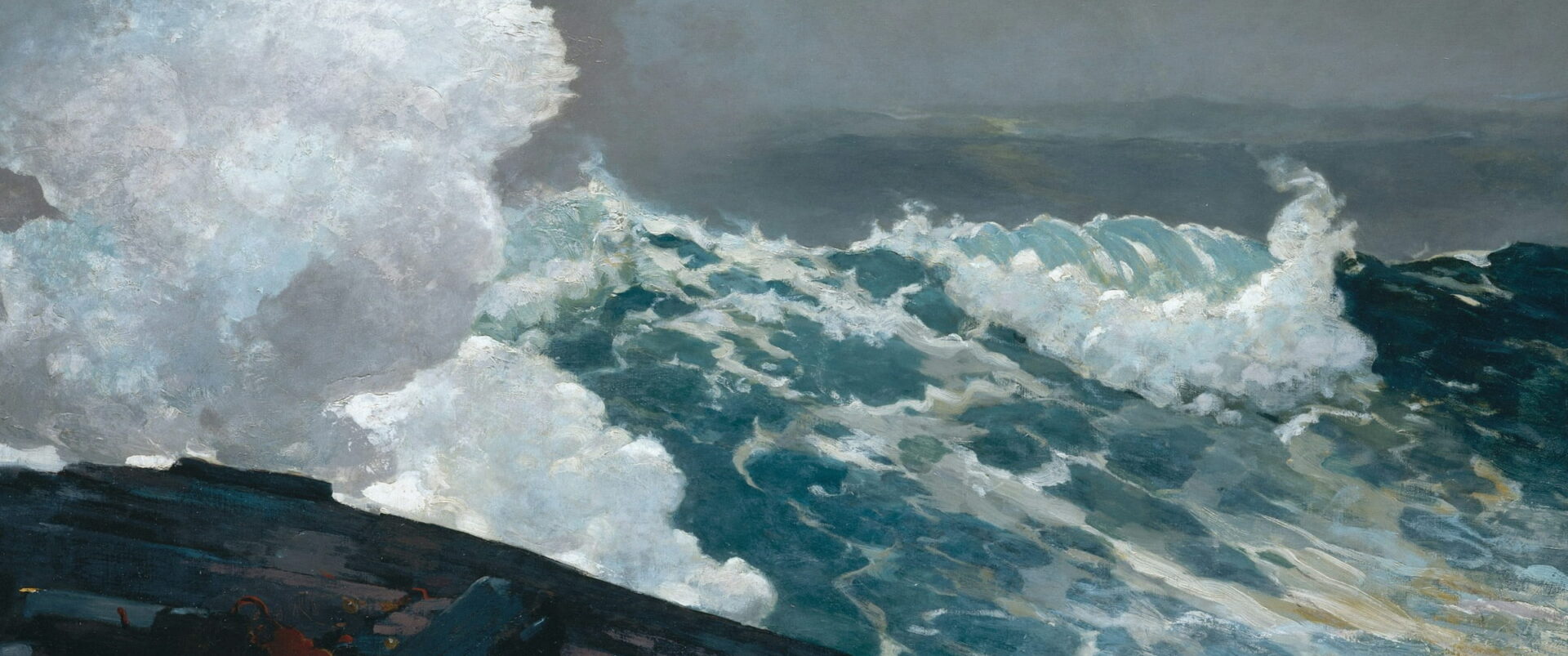 A wave bursts white over a black rock ledge under a gray sky.