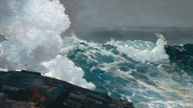 A wave bursts white over a black rock ledge under a gray sky.