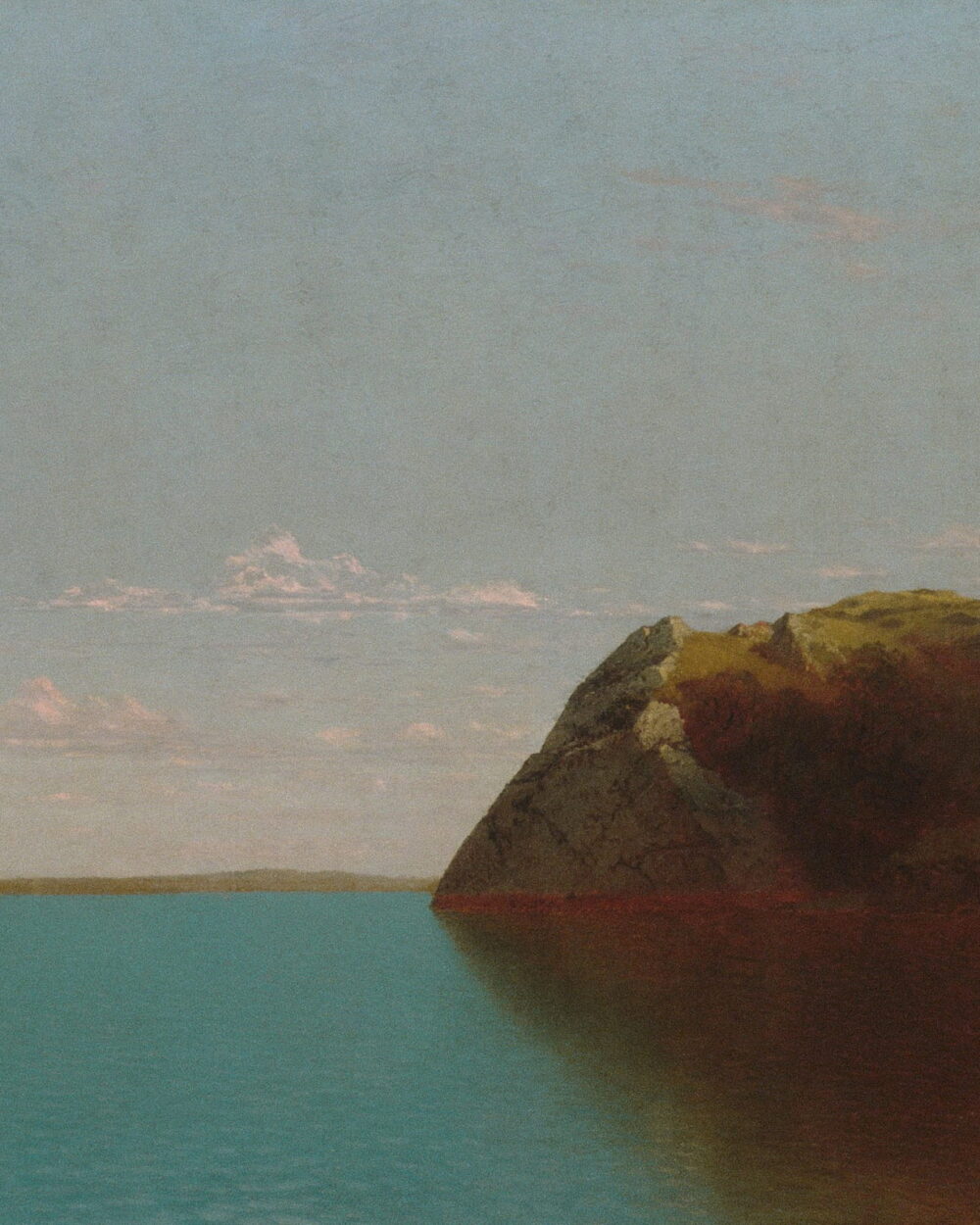 A red rock headland reaches into flat blue water under a pale sky.