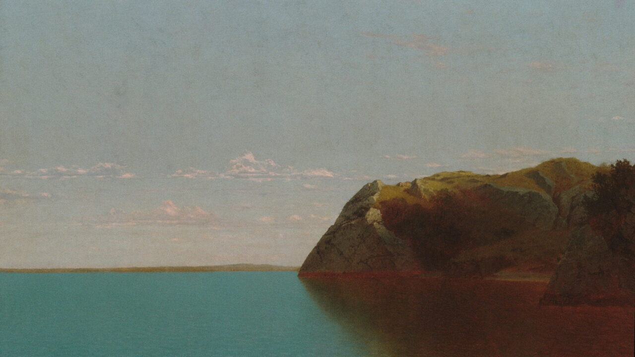 A red rock headland reaches into flat blue water under a pale sky.