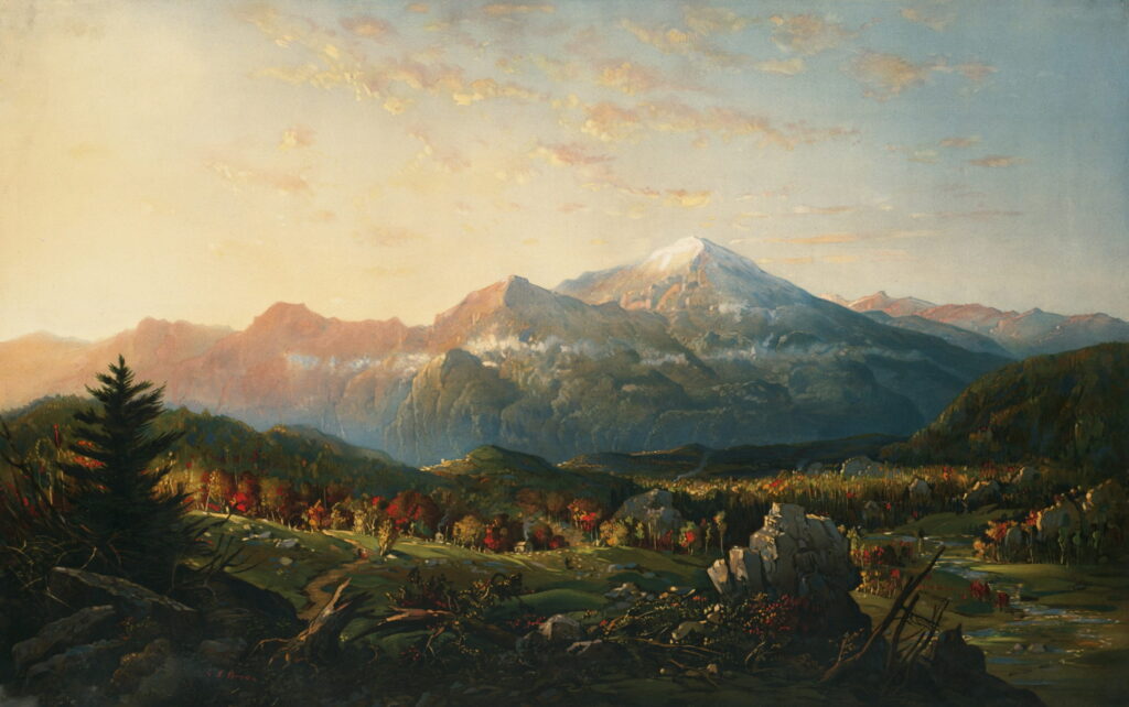 Morning light reaches a snowy peak above an autumn valley.