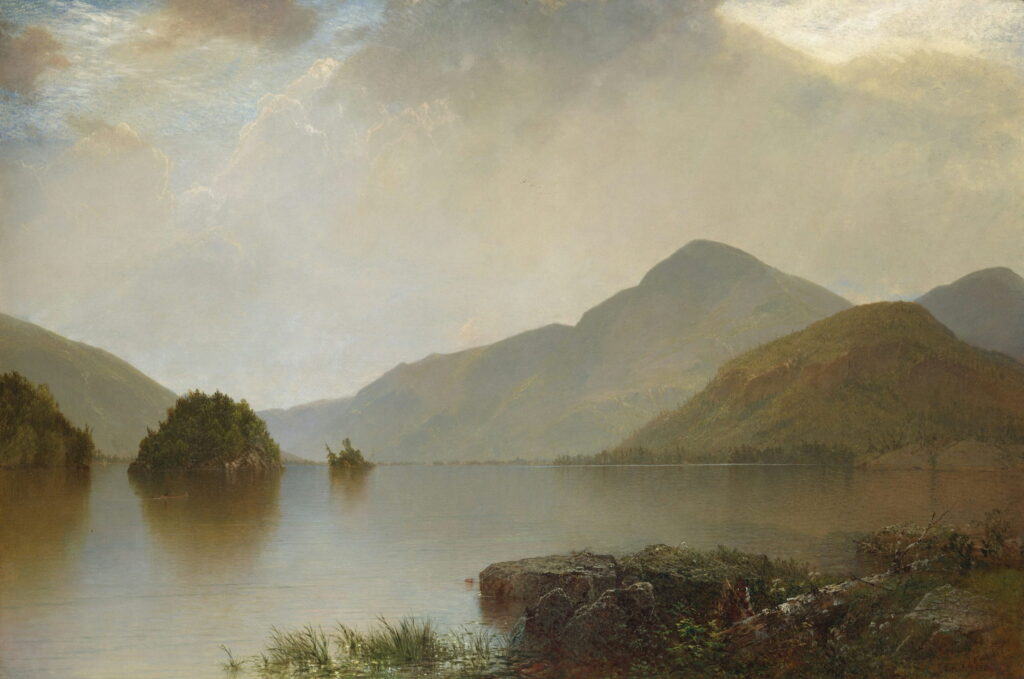A calm lake with small wooded islands below hazy mountains.