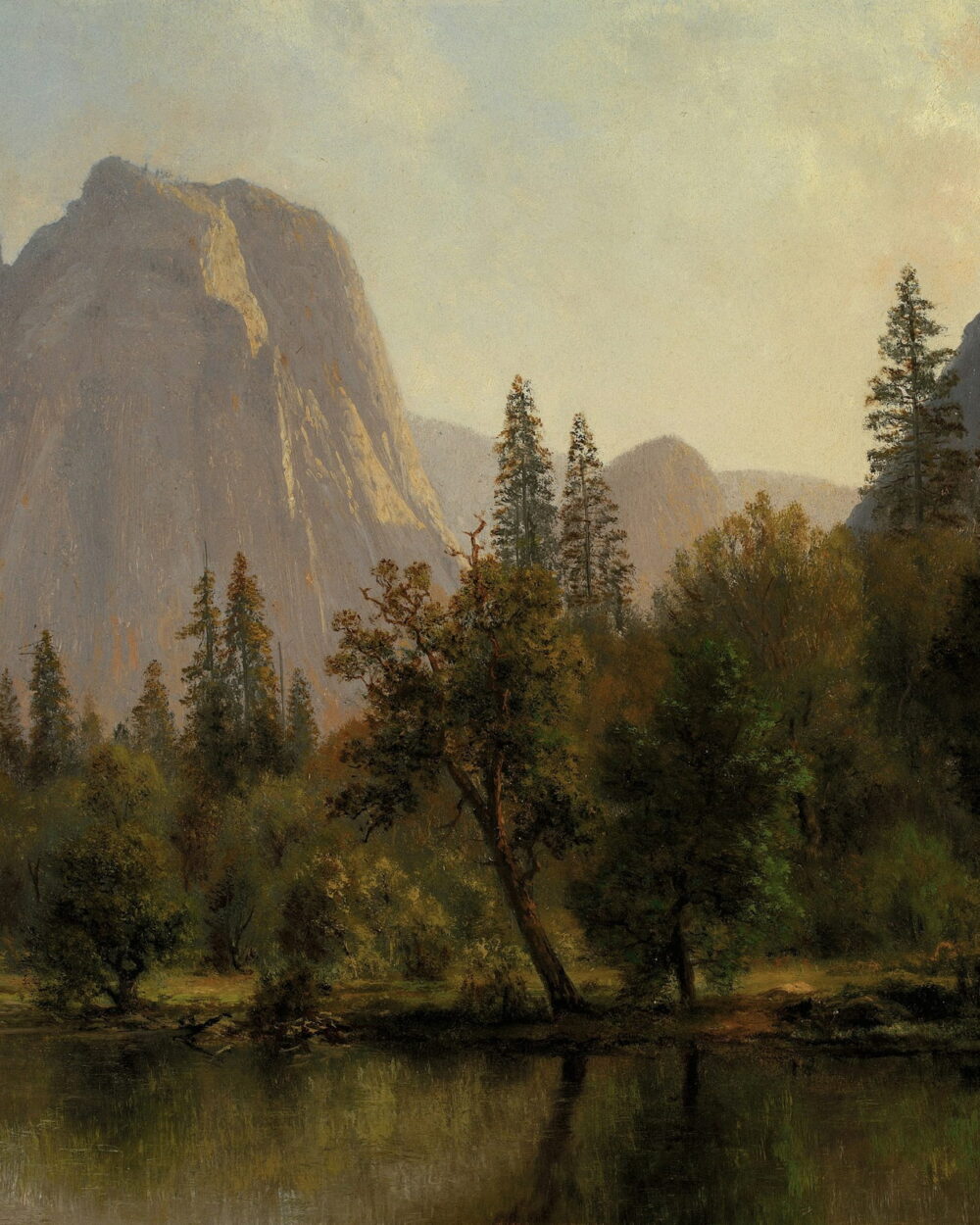 Tall pines stand by a still lake below gray granite cliffs.