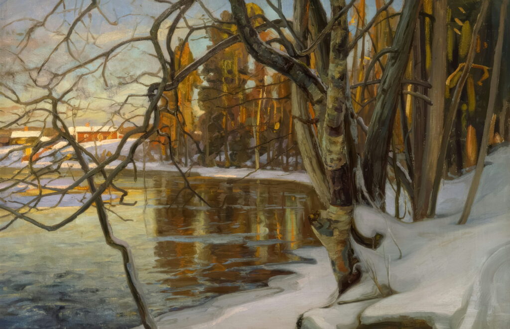 A calm winter river with snow on the bank and bare trees in low sun.