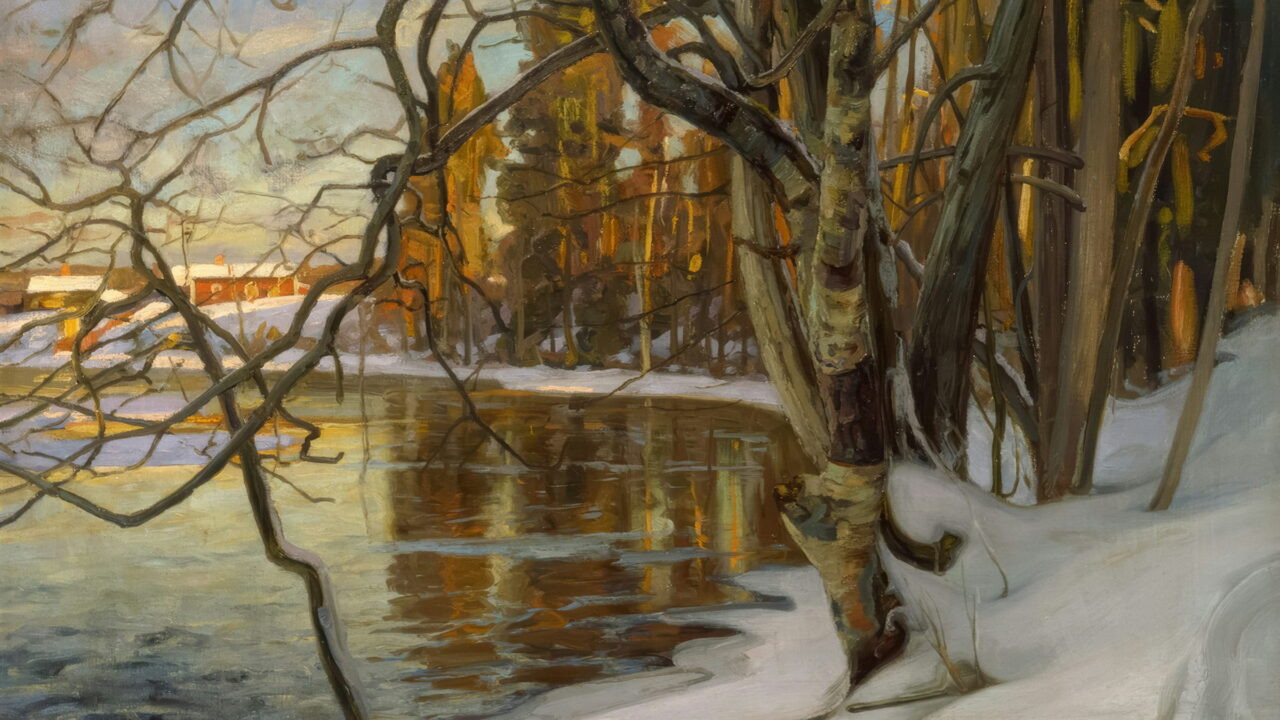 A calm winter river with snow on the bank and bare trees in low sun.