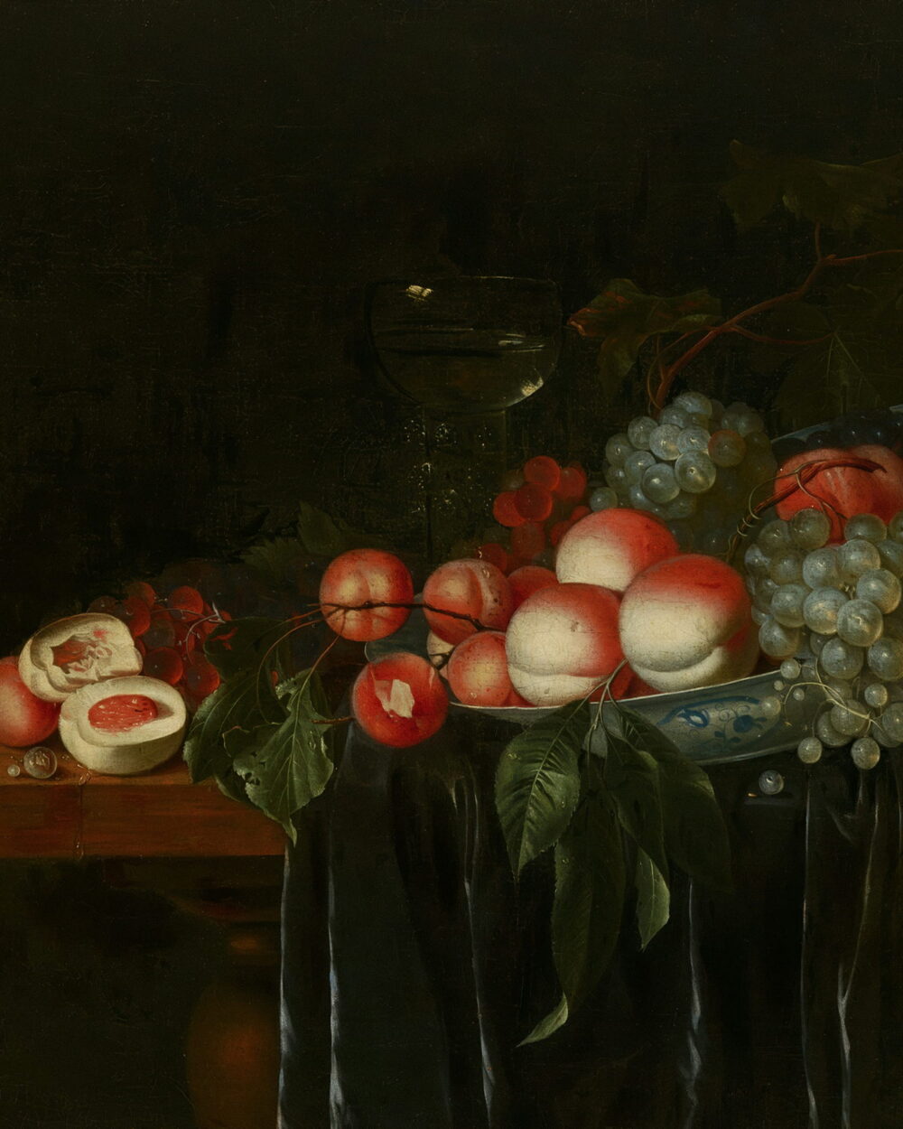 Peaches and grapes on a blue and white plate at the edge of a green cloth.