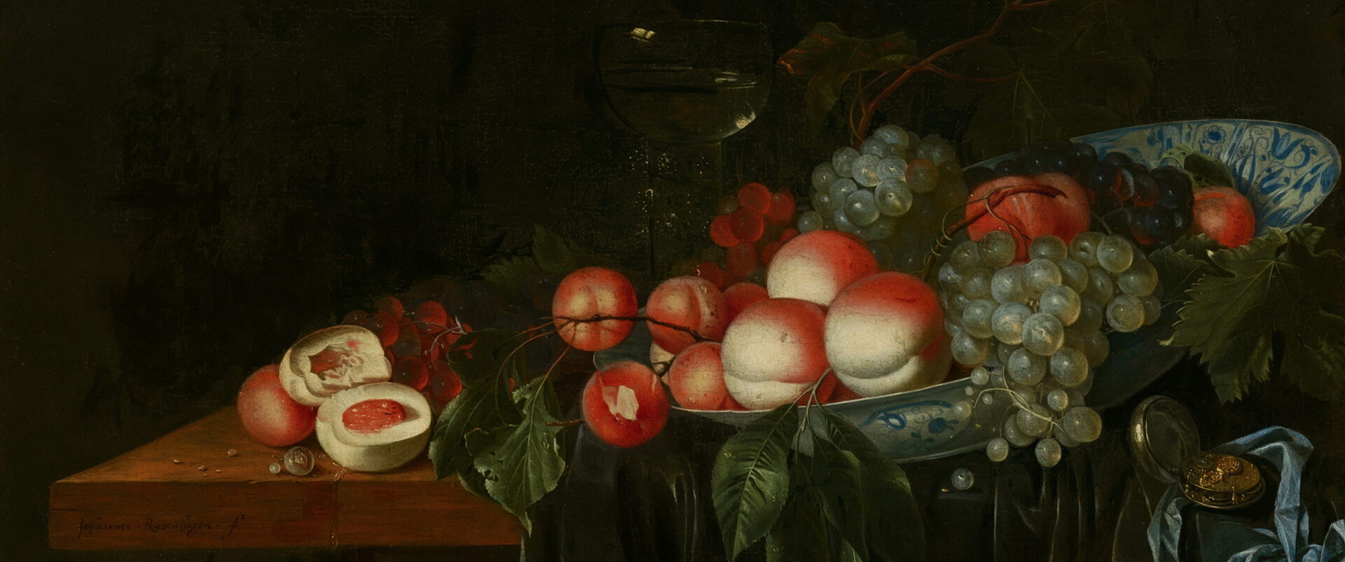 Peaches and grapes on a blue and white plate at the edge of a green cloth.