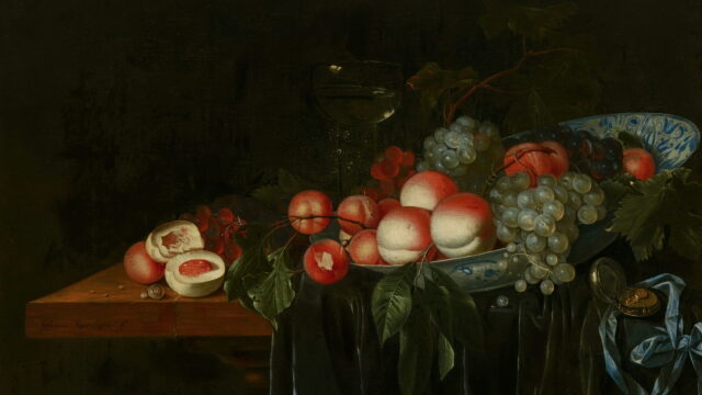 Peaches and grapes on a blue and white plate at the edge of a green cloth.