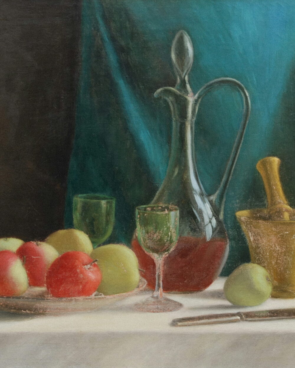 A glass decanter of red wine, apples on a plate, and a brass mortar on a white cloth.