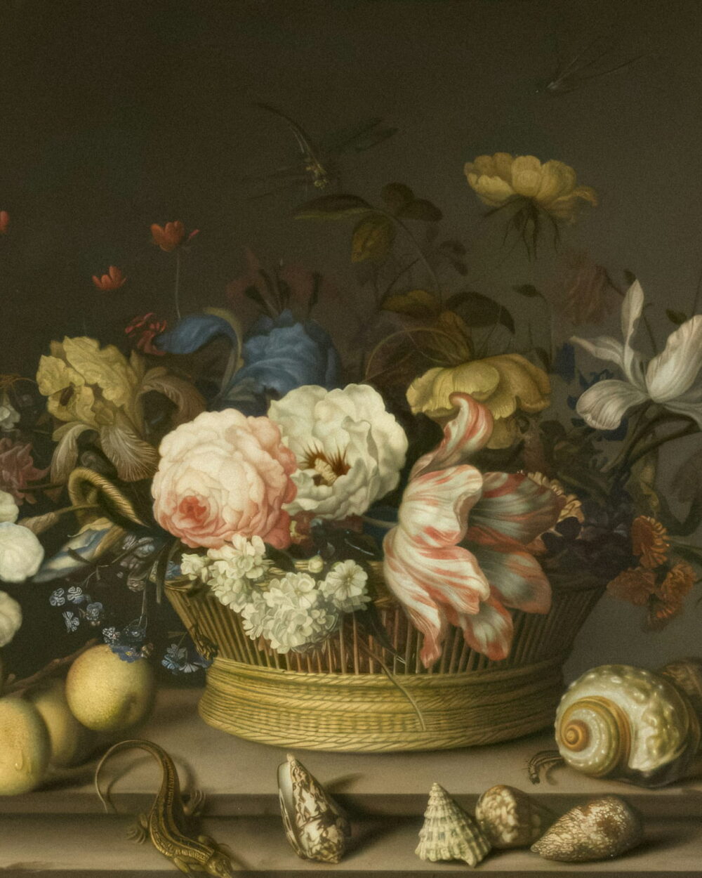 A basket of roses and tulips on a ledge with seashells laid out in front.