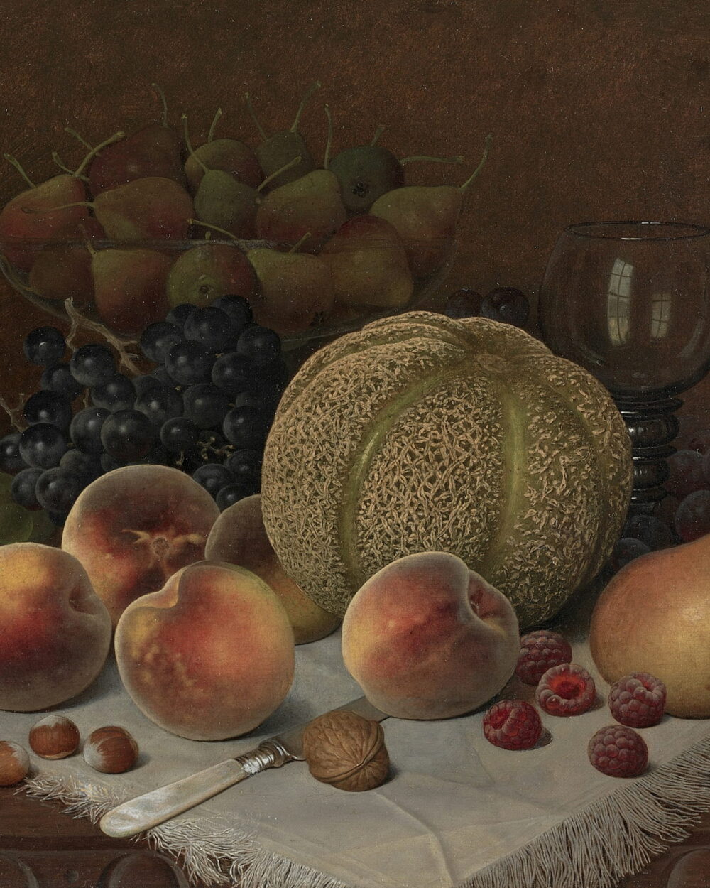 A cut melon, peaches, a pear, and grapes on a white cloth with a wine glass.