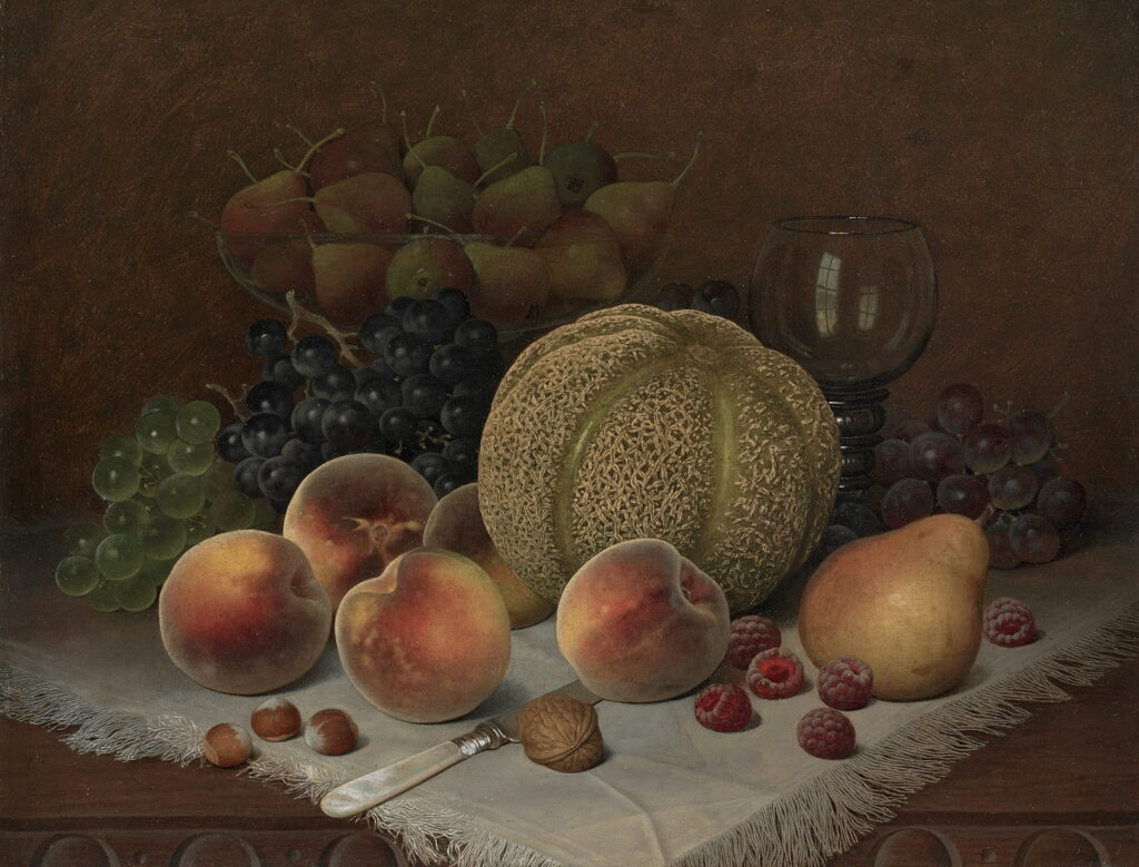 A cut melon, peaches, a pear, and grapes on a white cloth with a wine glass.