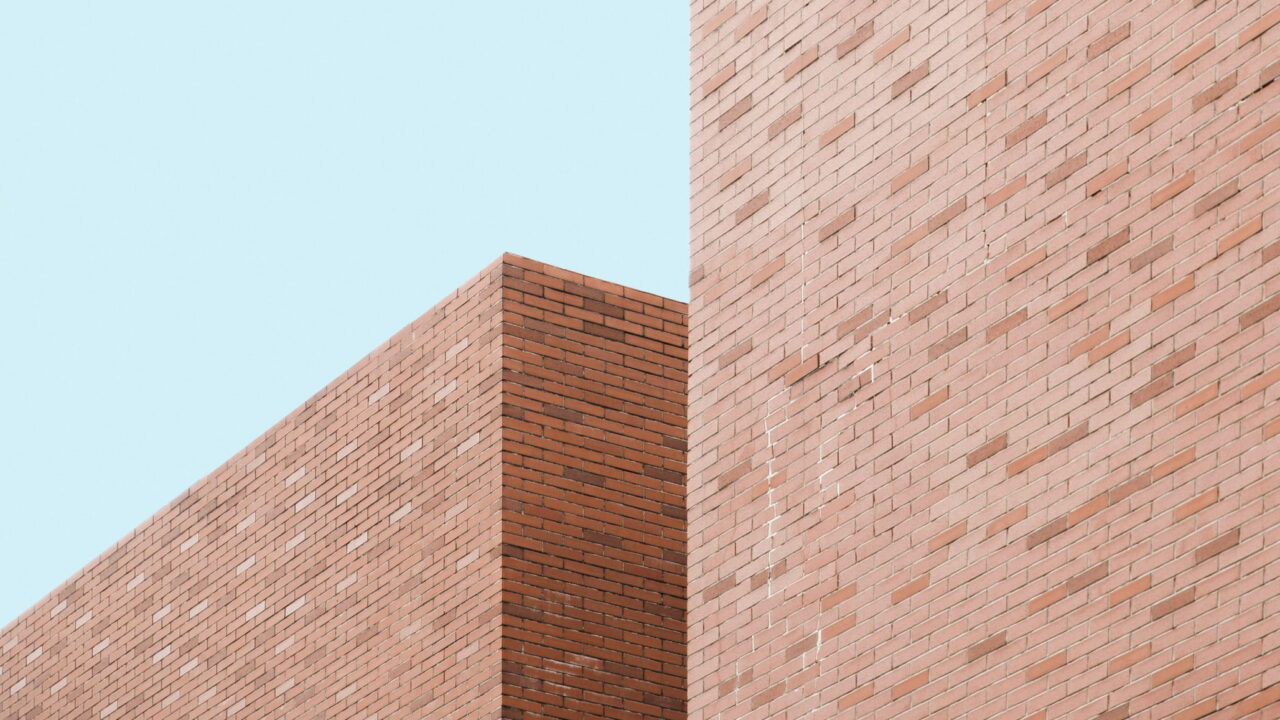 Two brick walls meeting at a corner against a pale blue sky.
