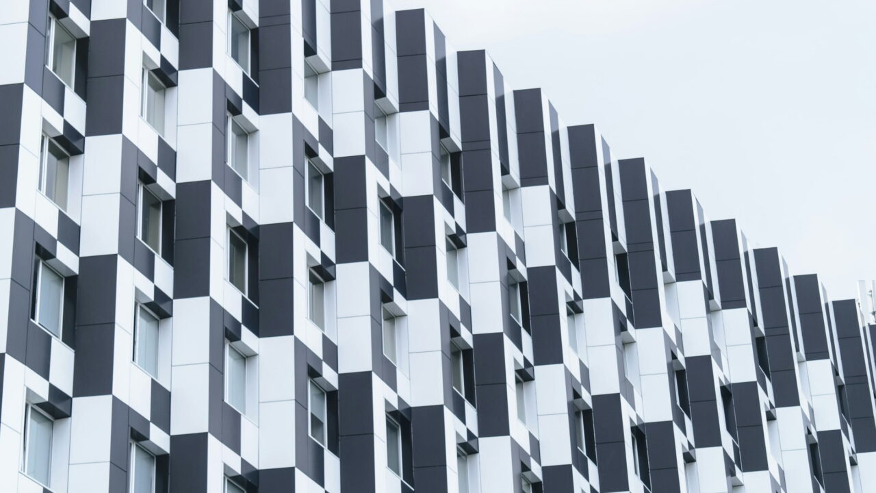 A white apartment block with a checker pattern of dark window frames against a pale sky.