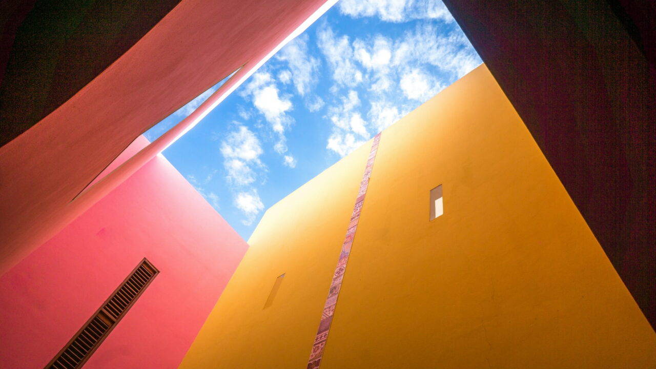 Red and yellow walls framing a patch of blue sky, seen from below.