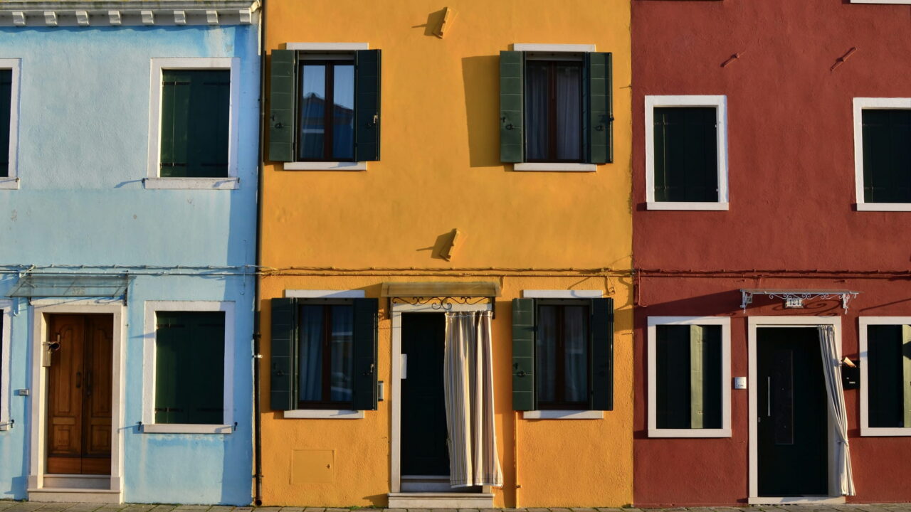 A row of blue, yellow, and red painted houses with open doors.