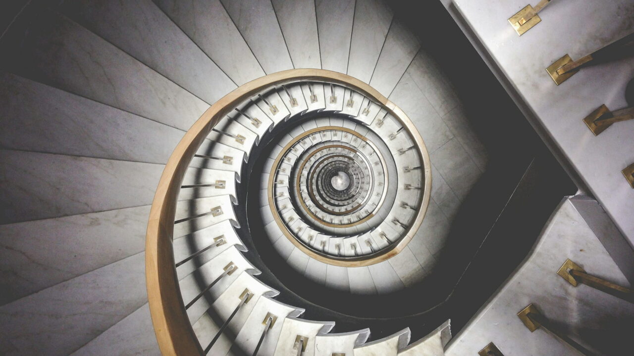 A white spiral staircase seen from below, curling into a tight center.