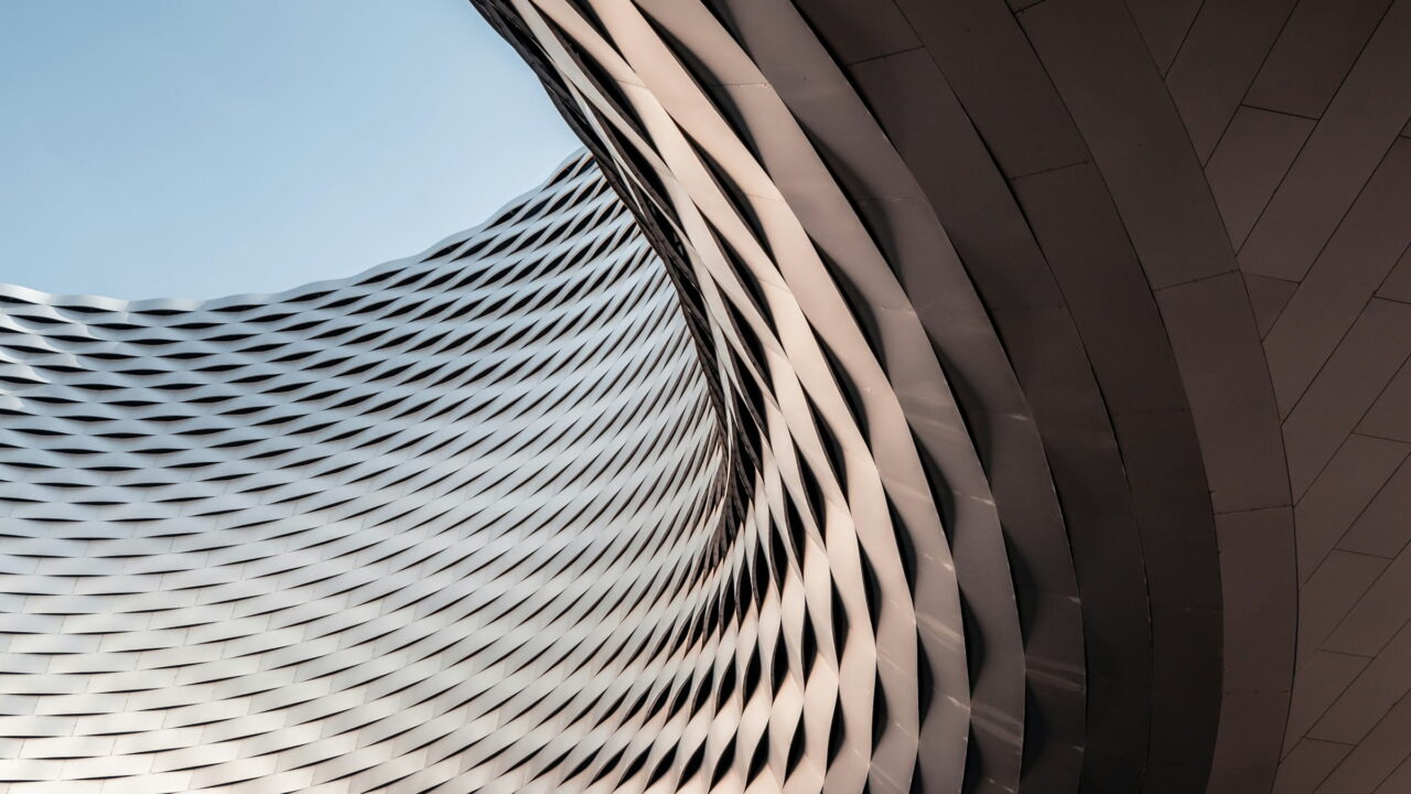 A curved metal facade woven like a basket, against a clear sky.