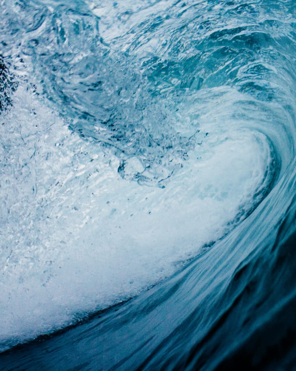 The inside of a curling blue wave, lit from behind.