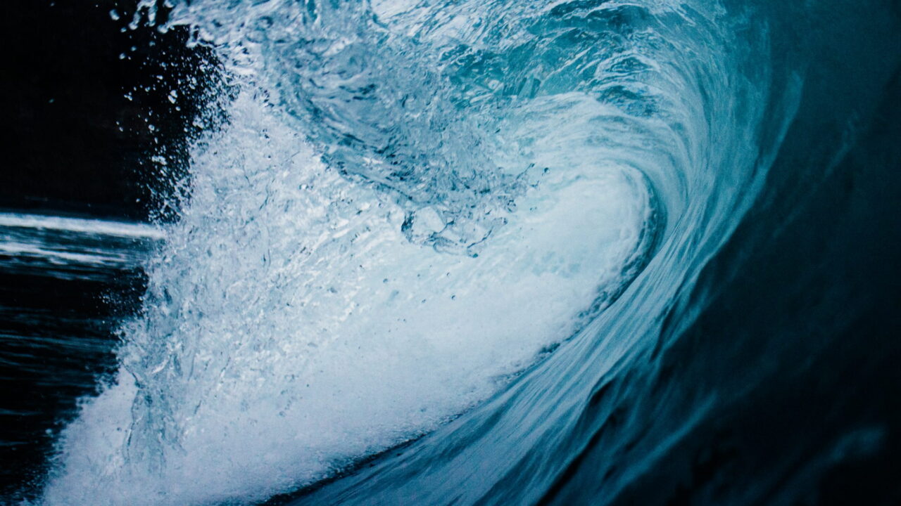 The inside of a curling blue wave, lit from behind.