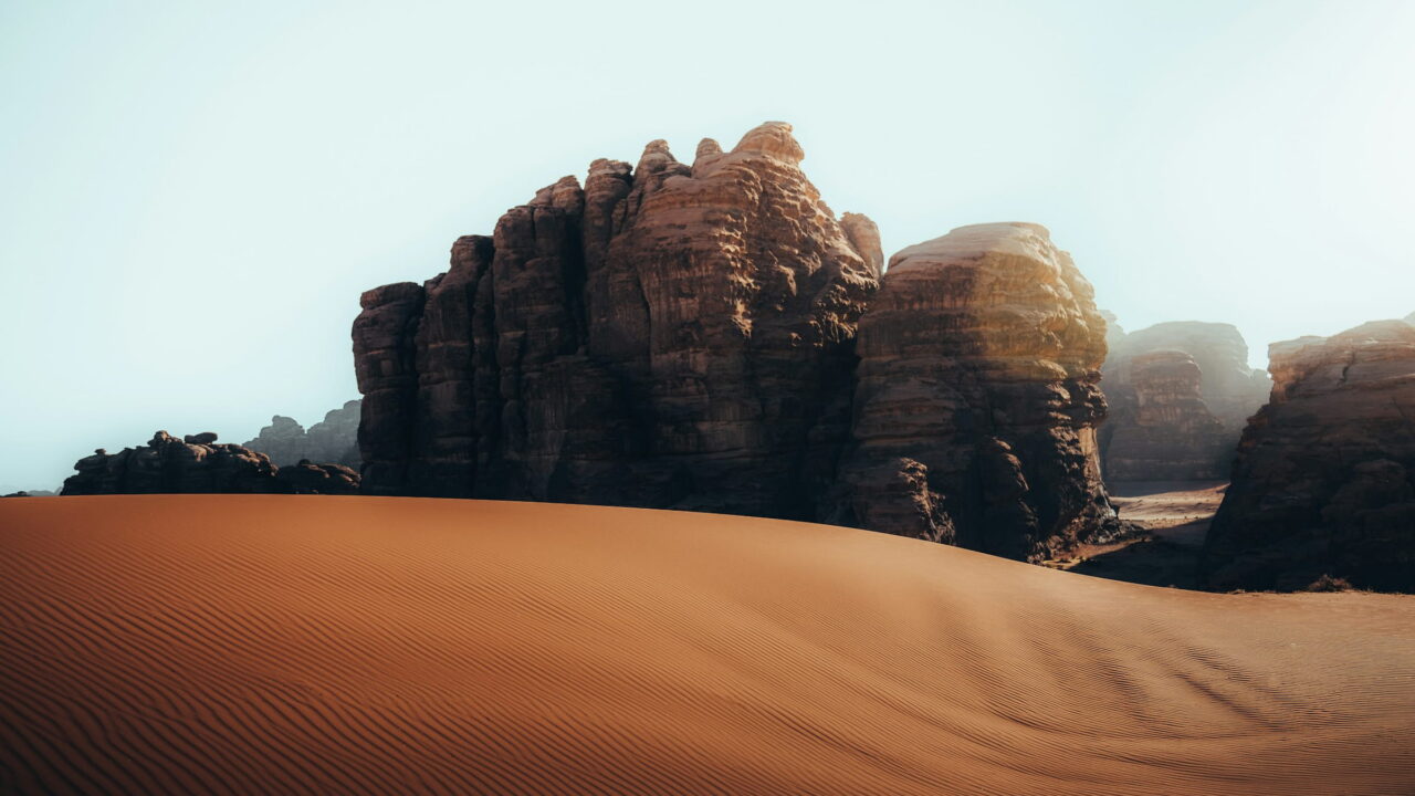 A smooth sand dune in front of tall, weathered rock towers.