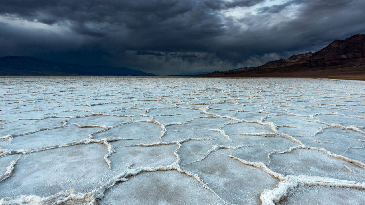 A white salt flat cracked into shapes under a dark storm sky.