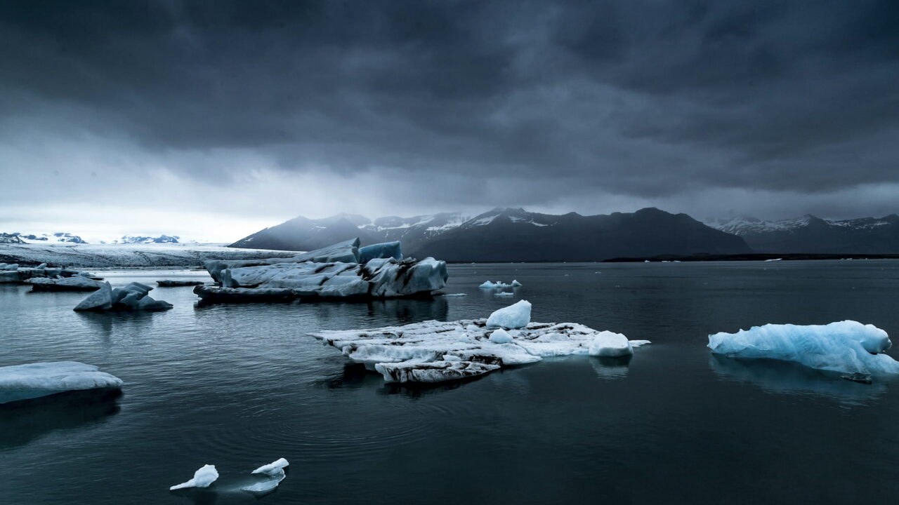 Blue and white icebergs floating in a dark lagoon under a heavy storm sky.
