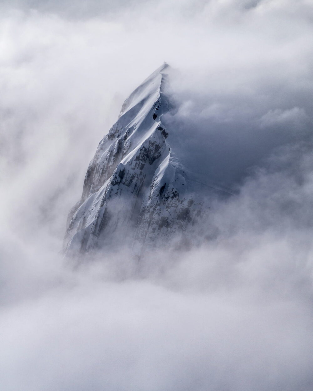 A sharp rock spire breaking through a thick sea of cloud.