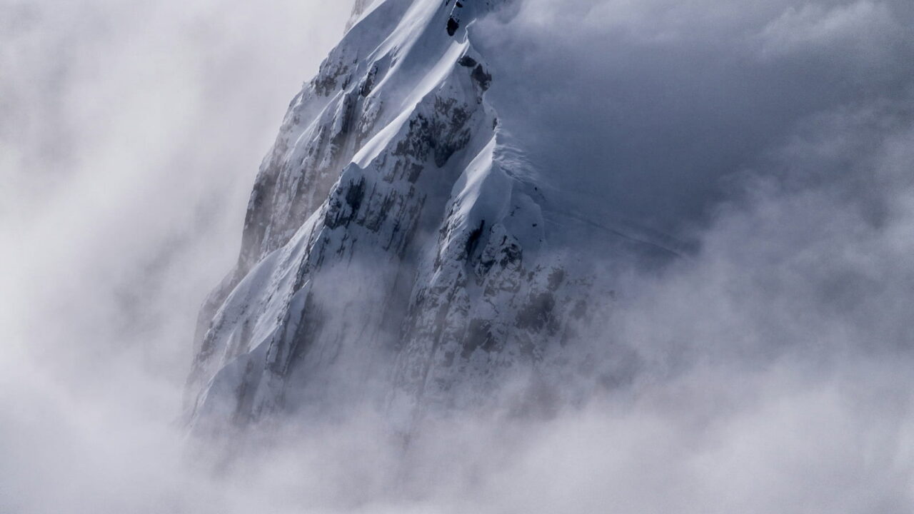 A sharp rock spire breaking through a thick sea of cloud.