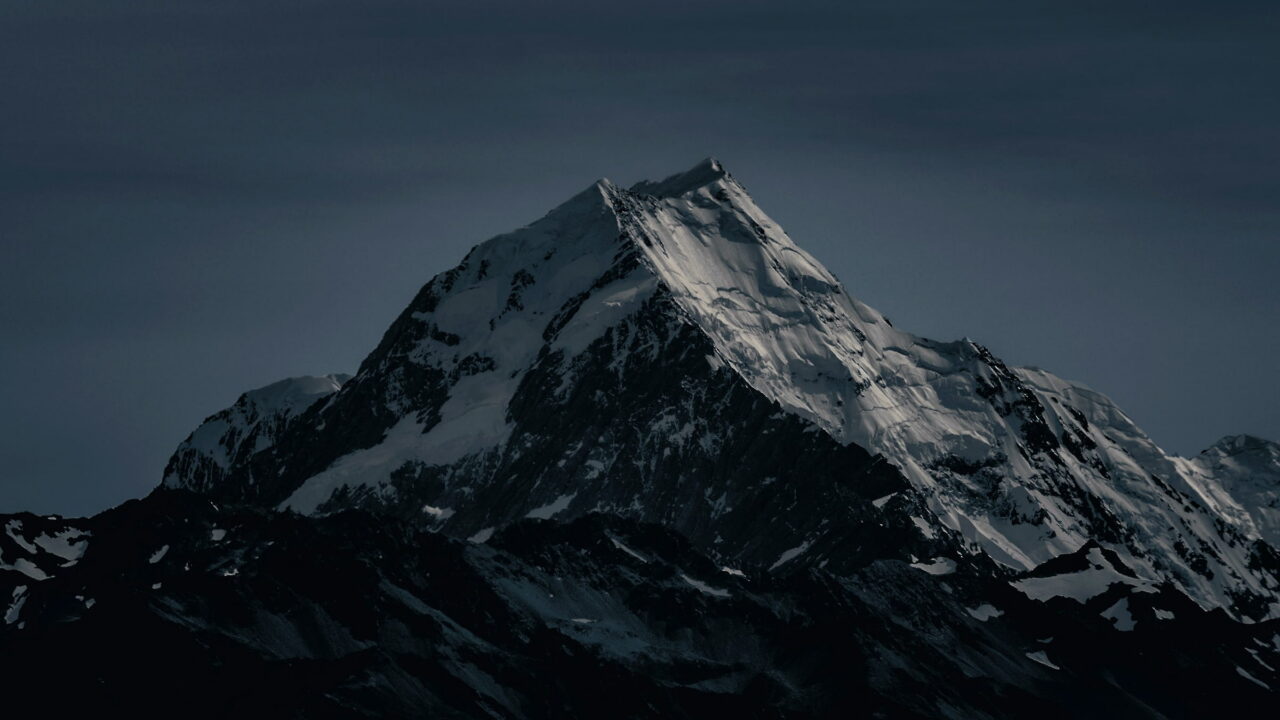 A snow-covered pyramid peak against a dark gray sky.
