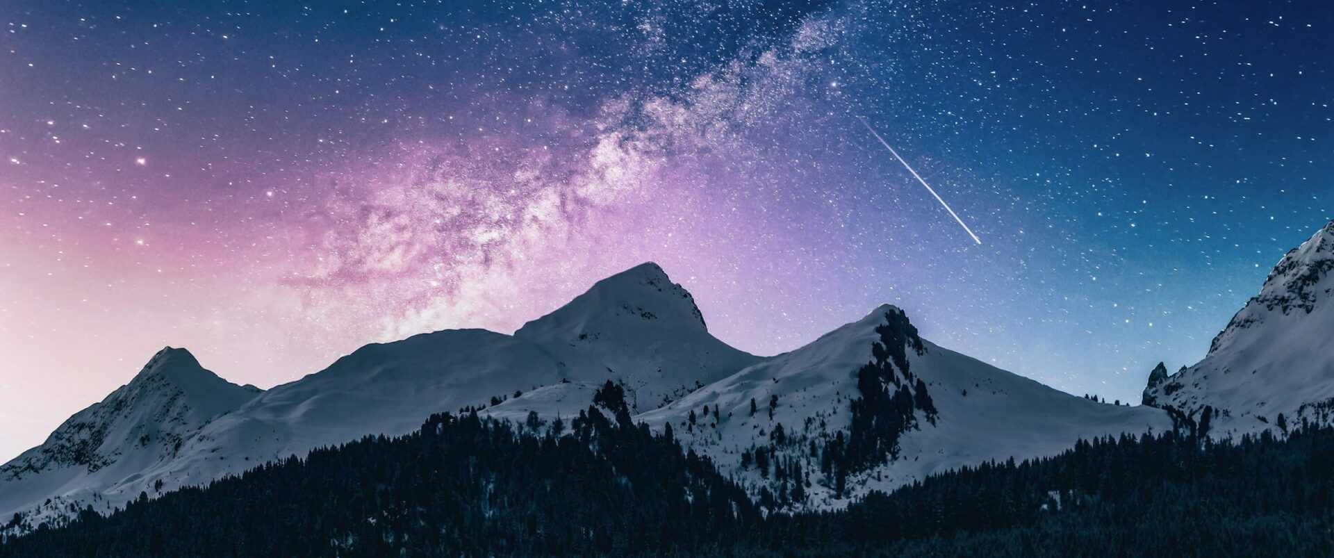 The Milky Way rising in a violet sky over snowy peaks and a dark forest.