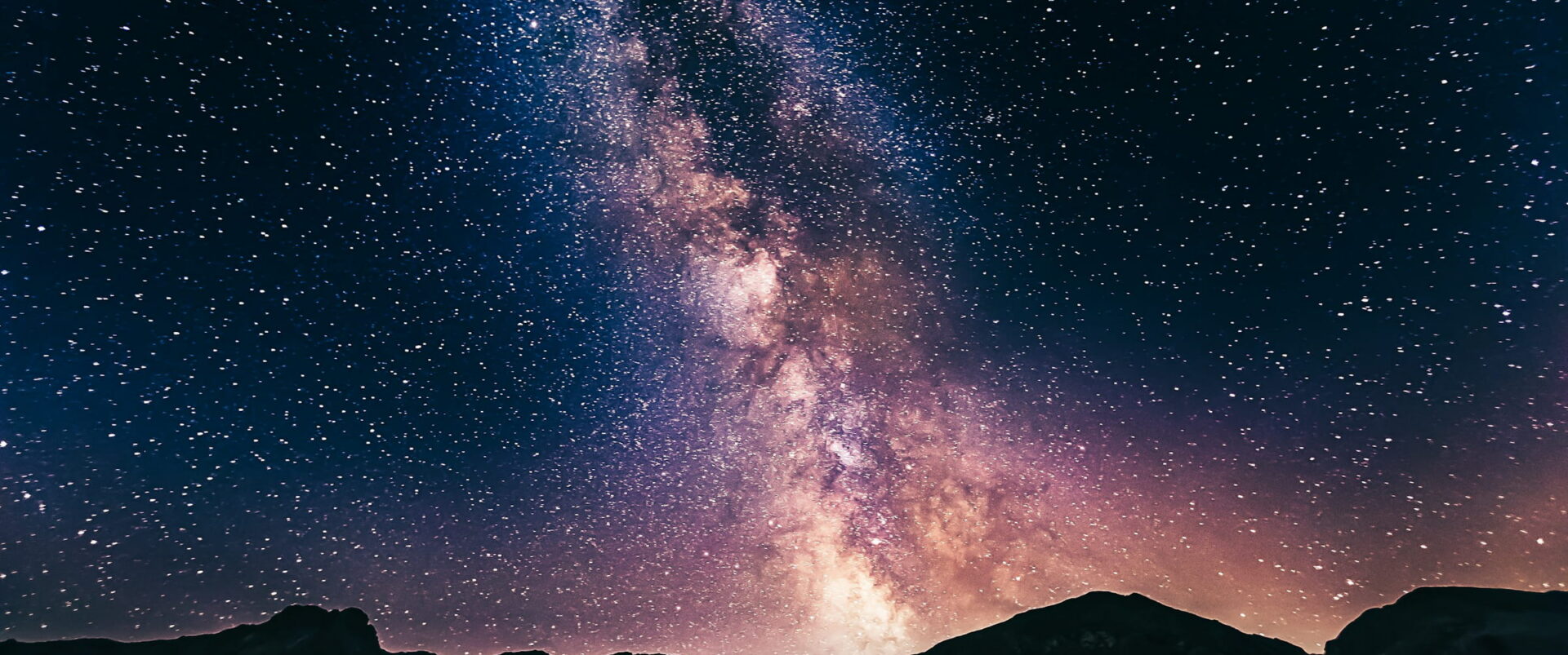 The bright core of the Milky Way standing above a rocky mountain ridge.