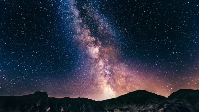The bright core of the Milky Way standing above a rocky mountain ridge.